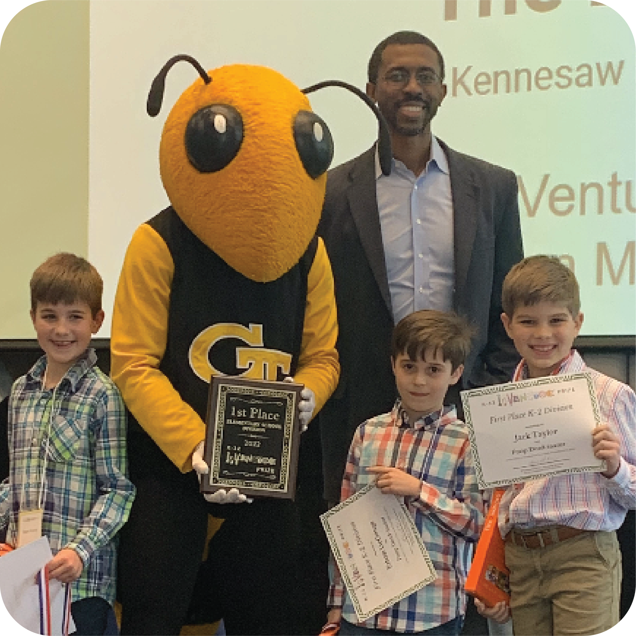 Three smiling students holding prizes and standing next to Buzz (Georgia Tech's yellowjacket mascot) holding a plaque and Craig Cupid (Georgia Intellectual Property and Alliance representative).